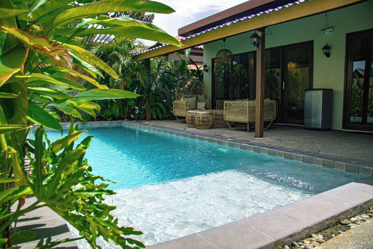 A swimming pool with wicker chairs and a covered patio area.