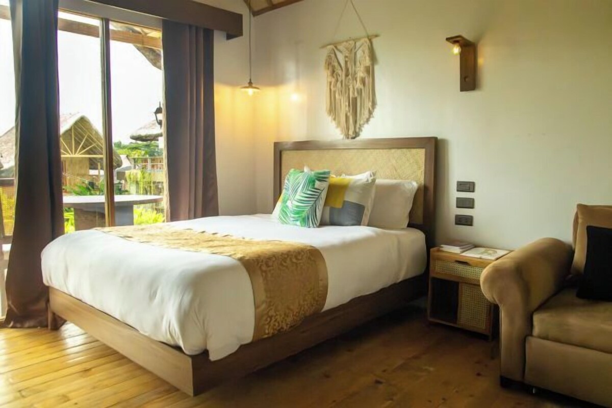 Un dormitorio con una cama grande, una mesita de noche, una silla y vistas al exterior.