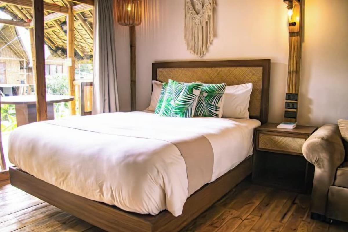 Una cama con estructura de madera, una mesita de noche con lámpara y vistas al exterior.