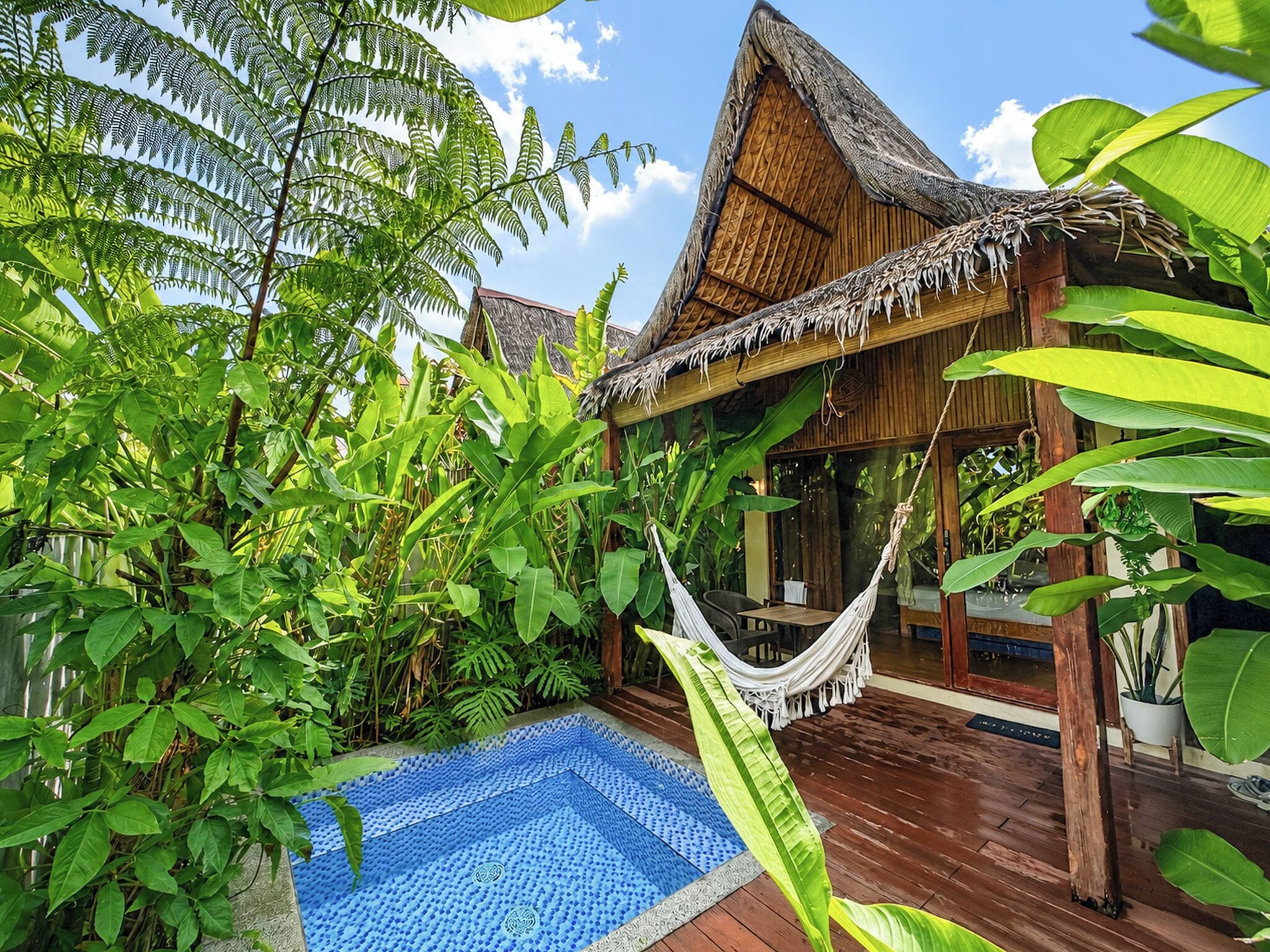 Un resort tropical con piscina, hamaca y exuberante vegetación.