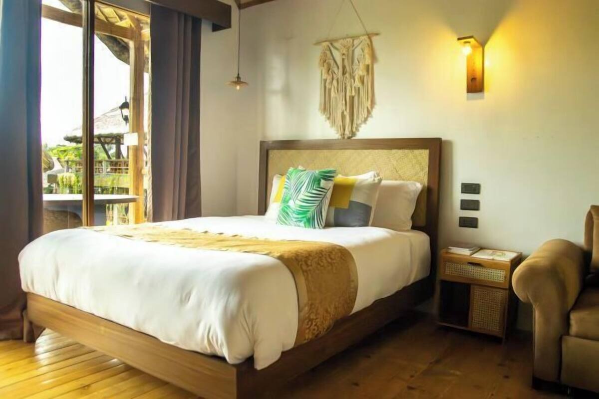 Un dormitorio con una cama de madera, una mesita de noche, una silla y una lámpara fijada a la pared.