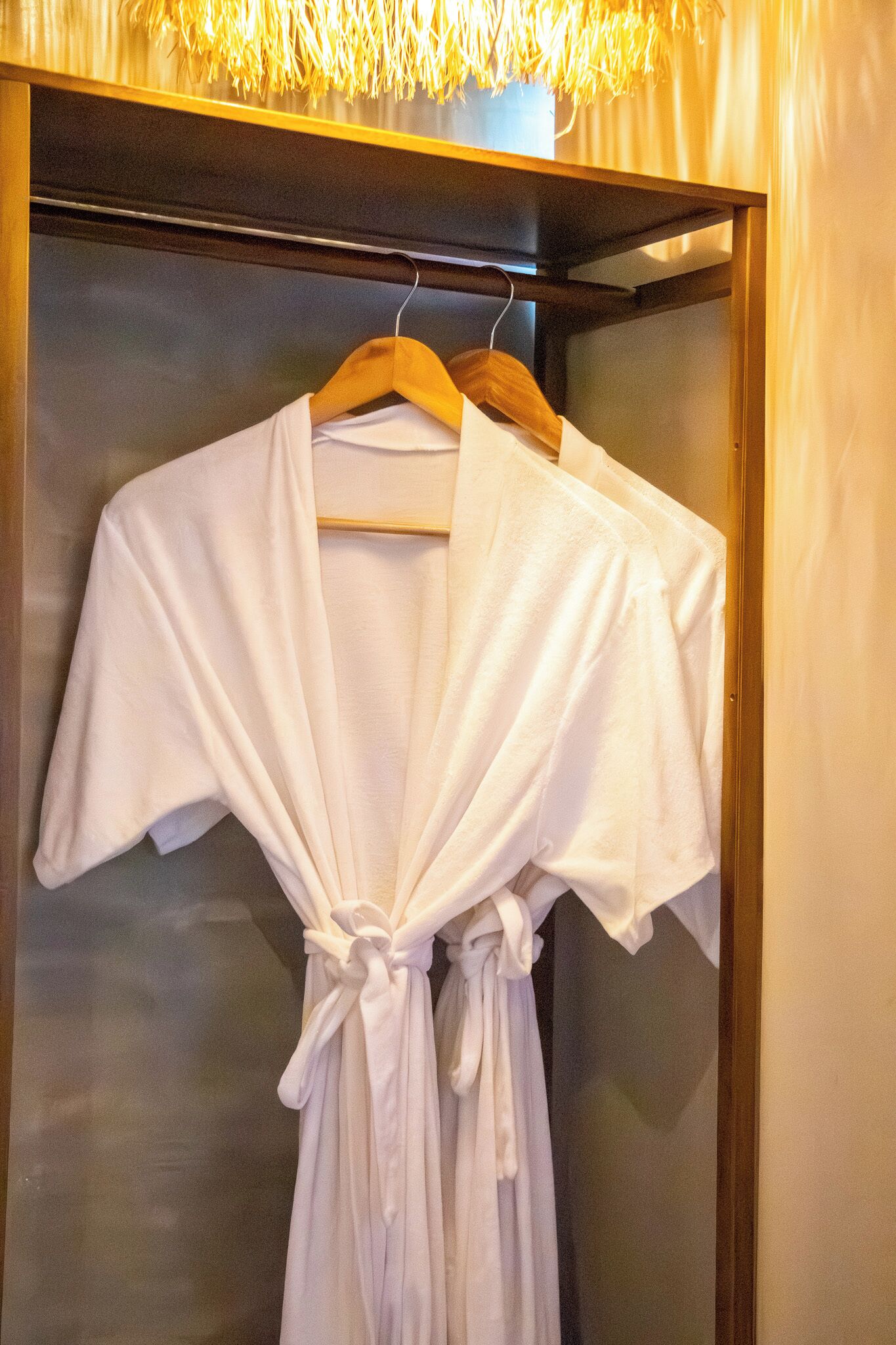 A white robe hanging on a wooden hanger in a closet with a glass door.