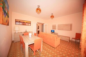 A room with a dining table, orange sofa, and a TV. - Crispi 231 - Milanomare (Pietra Ligure)