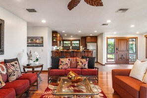 A spacious living room with a red sofa, a glass coffee table, and a dining area with wooden cabinets and a large window.