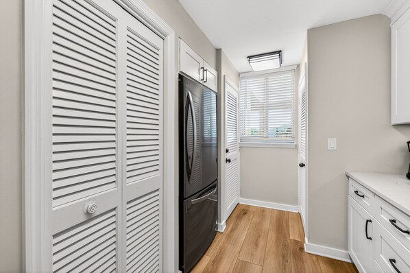 A kitchen with white cabinetry, a black refrigerator, and a window with blinds.