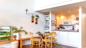 Una cocina moderna con armarios blancos, un microondas y una zona de comedor con sillas de madera y un televisor.