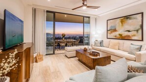 A modern living room with a sofa, coffee table, and TV. It features a large window with a city view and a ceiling fan. - Casa Kavita Mistiq | El Tezal Luxury Penthouse Condo (El Tezal)
