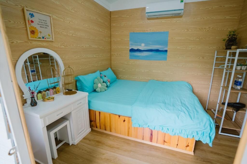 Ein Schlafzimmer mit einer Holzwand, einem Bett mit blauer Decke, einer weißen Kommode, einem Spiegel und einem Regal mit Pflanzen.