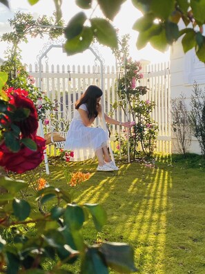 A person sitting on a bench in a garden with a white fence and greenery. - Hometa Homestay (Bao Loc)