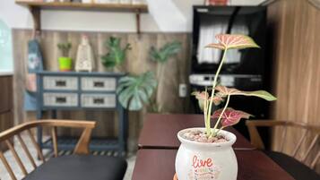 A dining table with a potted plant on a coaster, a television in the background, and a shelf with decorative items.