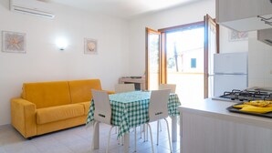 En kompakt opholdsstue med en gul sofa, et spisebord med ternet dug og et køkkenområde med komfur.