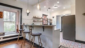 A kitchen with a bar area, wooden stools, a refrigerator, and a window with a view. - Old Florida Charm Arts District 3br Steps to River (Melbourne)