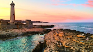 A coastal scene with a lighthouse, rocky shoreline, and calm sea.