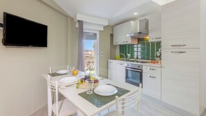 A modern kitchen with white cabinetry, a flat-screen TV mounted on the wall, and a dining area with a table set for two.