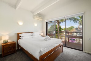 A bedroom with a wooden bed, a nightstand, and a large sliding glass door leading to an outdoor area with a view of palm trees and a pink car.