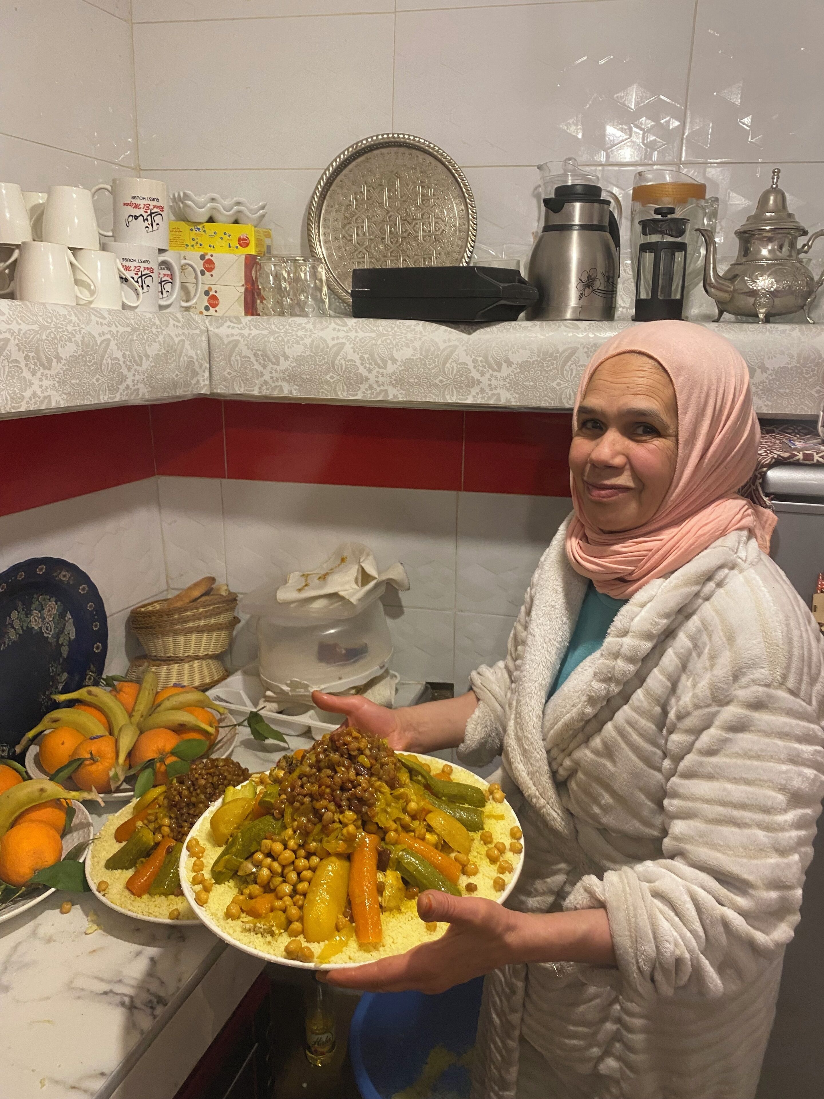 Uma cozinha com bancada de mármore, diversos utensílios e uma pessoa segurando um prato de comida.