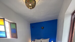 Una habitación con cama, pared azul, piso estampado y lámpara colgante.