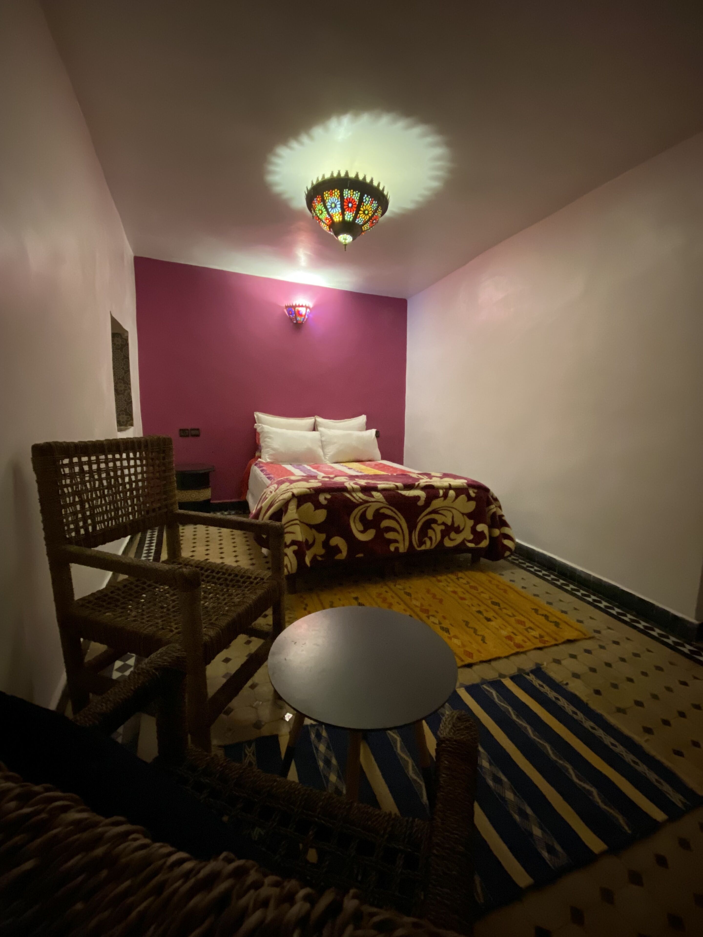 A room with a bed, a chair, a small table, and a decorative ceiling light.