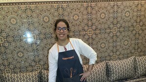 Una persona de pie detrás de una mesa con diversos alimentos y bebidas, como panqueques, huevos y una tetera.