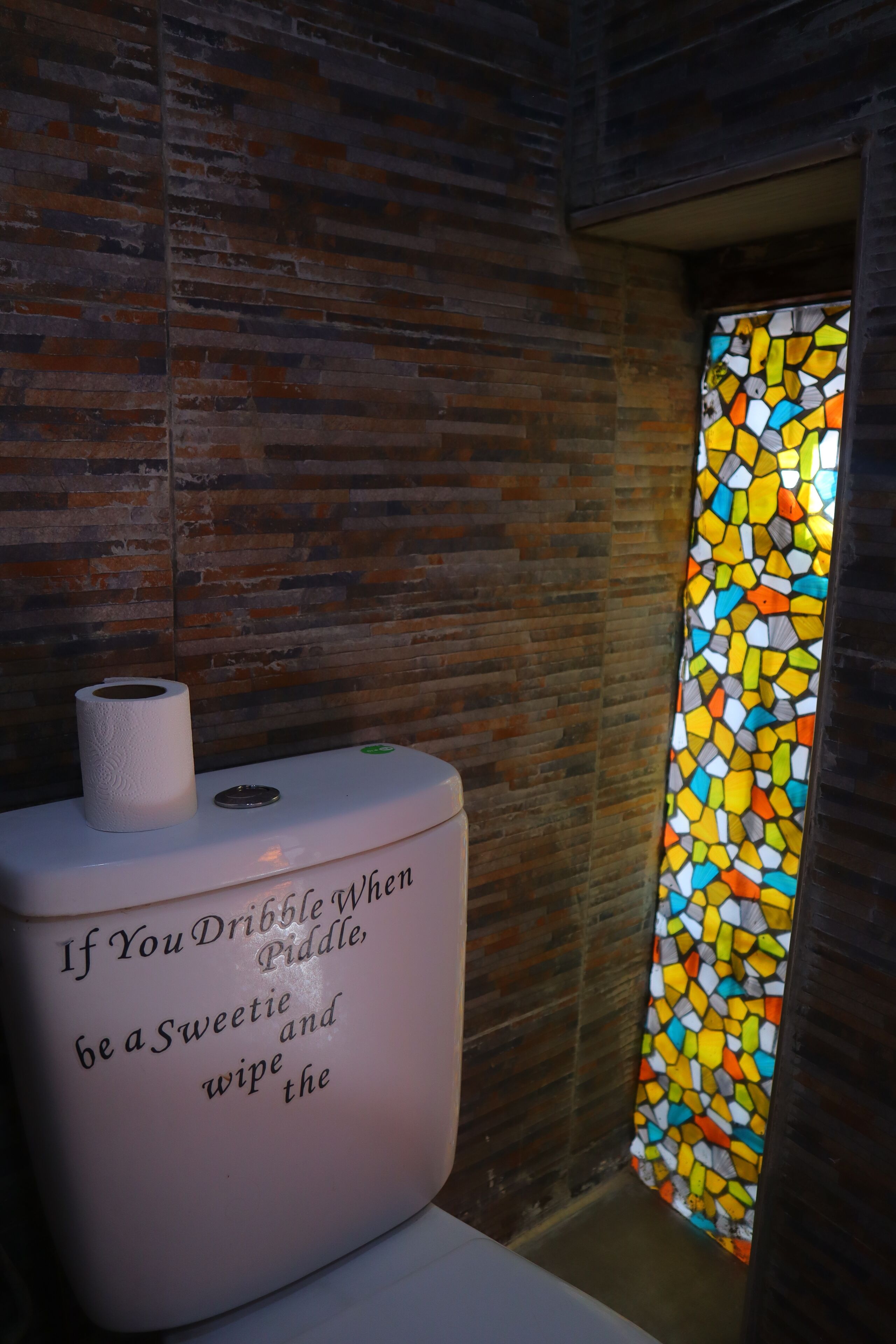 A bathroom with a white toilet, a roll of toilet paper, and a stained glass window.