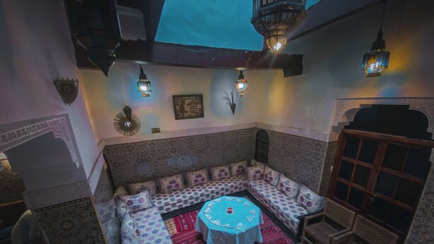 Una habitación acogedora con un sofá estampado, una mesita redonda y lámparas de pared tradicionales.