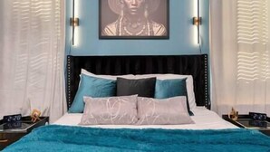 Een slaapkamer met een bed, kussens, een nachtkastje en een aan de muur bevestigd schilderij.