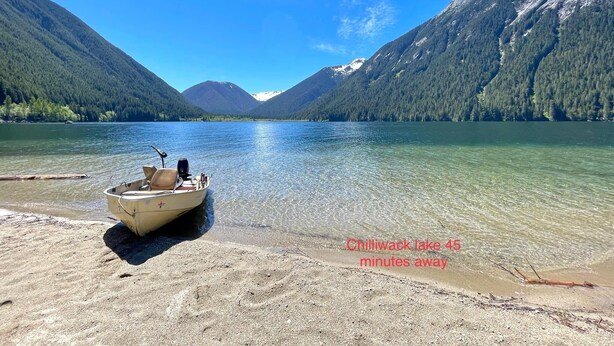 Ein Boot am sandigen Ufer mit freiem Blick auf einen See und Berge im Hintergrund.
