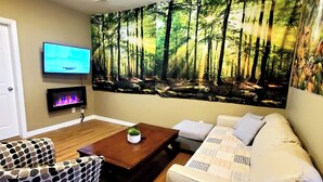 Ein Wohnzimmer mit einer großen Wandmalerei zum Thema Wald, einem Flachbildfernseher, einem Couchtisch, einer Couch und gemusterten Sesseln.