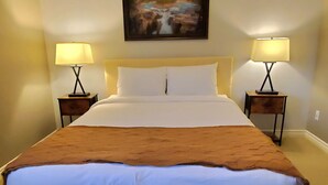 Ein ordentlich bezogenes Bett mit brauner Tagesdecke, zwei Nachttische mit Lampen und ein Bild an der Wand.