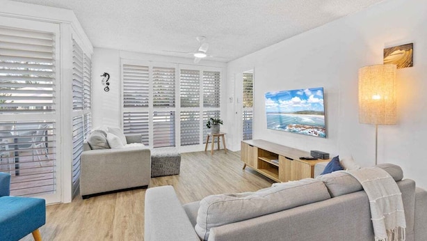 A modern living room with a sofa, TV, and a lamp. - Ocean and Pool Views from Beachside Apartment! (Gold Coast)
