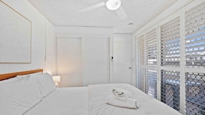 A hotel room with a bed, a ceiling fan, a door, and a window with blinds. - Ocean and Pool Views from Beachside Apartment! (Gold Coast)