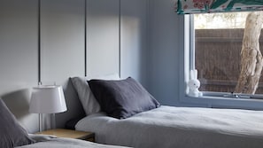 Un dormitorio con cama, mesita de noche, lámpara y ventana con vista a un árbol.