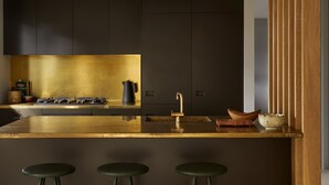 Eine moderne Küche mit dunklen Schränken, einer goldenen Arbeitsplatte und einer Bar mit Hockern.