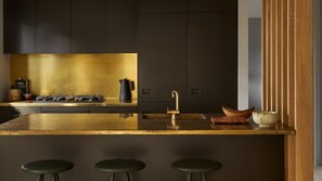 A modern kitchen with dark cabinetry, a gold countertop, and a bar area with stools.