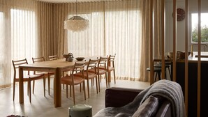 Ein Essbereich mit Holztisch, Stühlen, einer Chandelierleuchtre und Blick durch leichte Vorhänge.