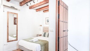 A bedroom with a bed, wooden beams, a large mirror, a wardrobe, and a bedside table. - Nice duplex with terrace feria street (Sevilla)