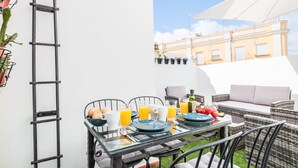 A glass table set with plates, glasses, and cutlery, surrounded by wicker chairs and a cushioned bench. - Nice duplex with terrace feria street (Sevilla)