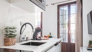 A modern kitchen with a white countertop, a black faucet, and a built-in oven. There is a window with wooden shutters and a view of buildings outside. - Nice duplex with terrace feria street (Sevilla)