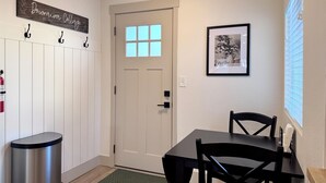 A room with a white door, a framed picture on the wall, a black table with chairs, and a trash bin.