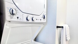 A front-loading washing machine with control knobs and a white towel hanging on a towel rack.