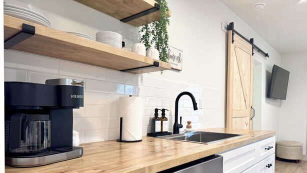 A modern kitchen with a coffee maker, dishwasher, wooden shelves, and a sliding door.