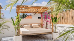 Een slaapkamer met een bed onder een houten pergola, potplanten en een kamer met een patroon op de vloer.