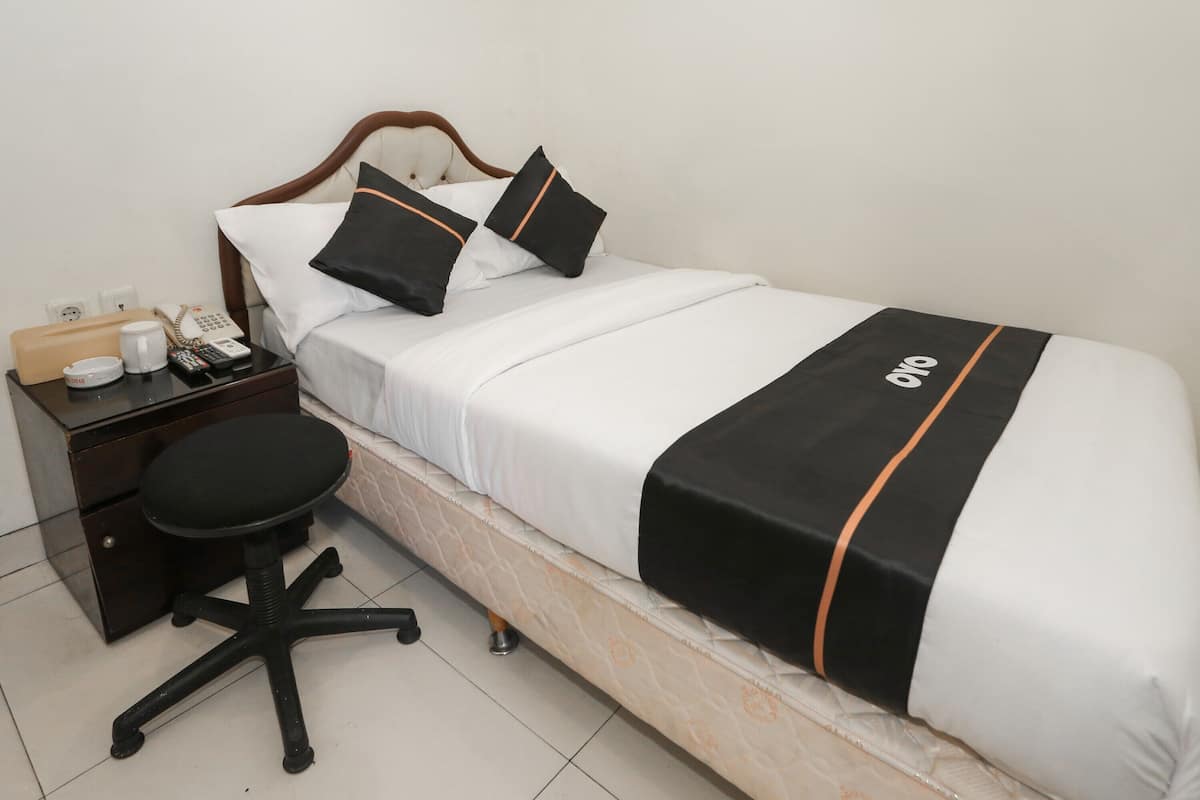 A neatly made bed with a black and white bedspread, a wooden headboard, and a bedside table with a telephone, a remote control, and a small lamp.