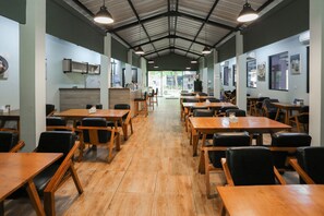 Un espacio interior amplio con varias mesas y sillas de madera, un techo alto con vigas metálicas y paredes decoradas con cuadros enmarcados.