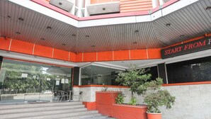 Entrada moderna de un edificio con fachada de vidrio, asientos al aire libre y un cartel que dice 