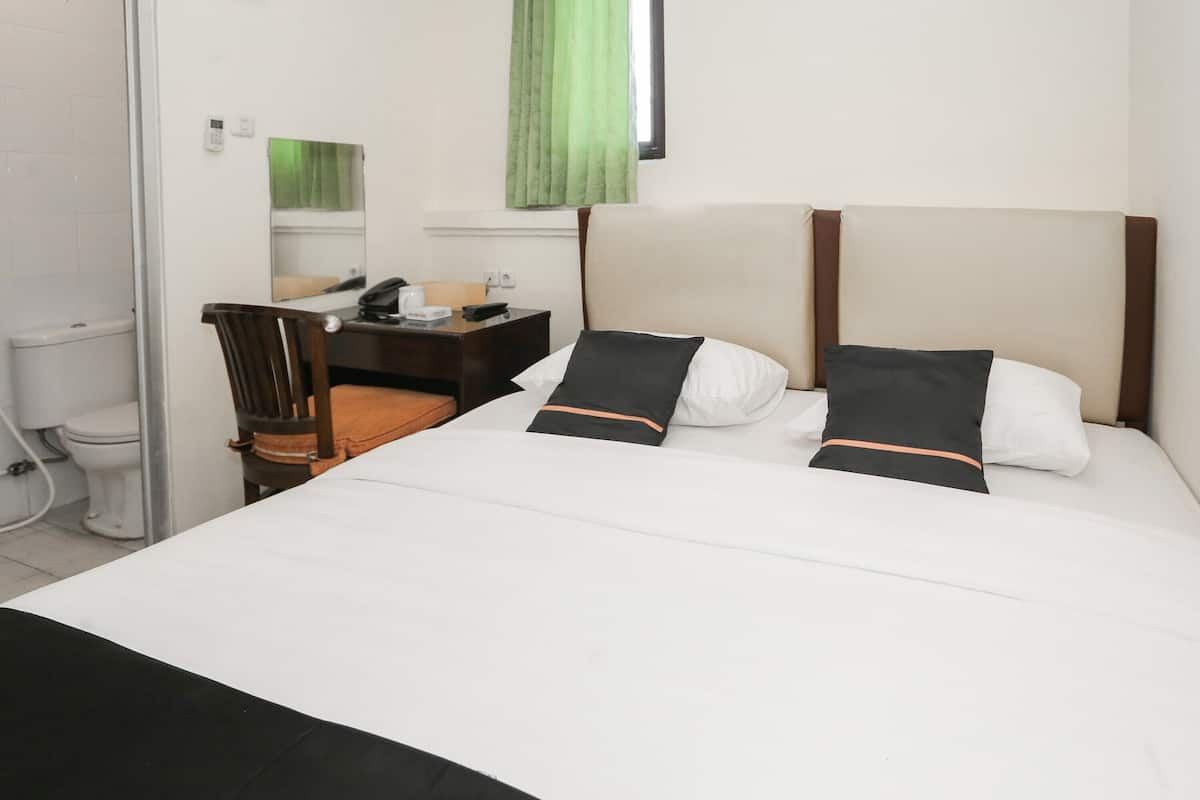 A hotel room with a bed, a desk, a chair, a toilet, and a window with curtains.