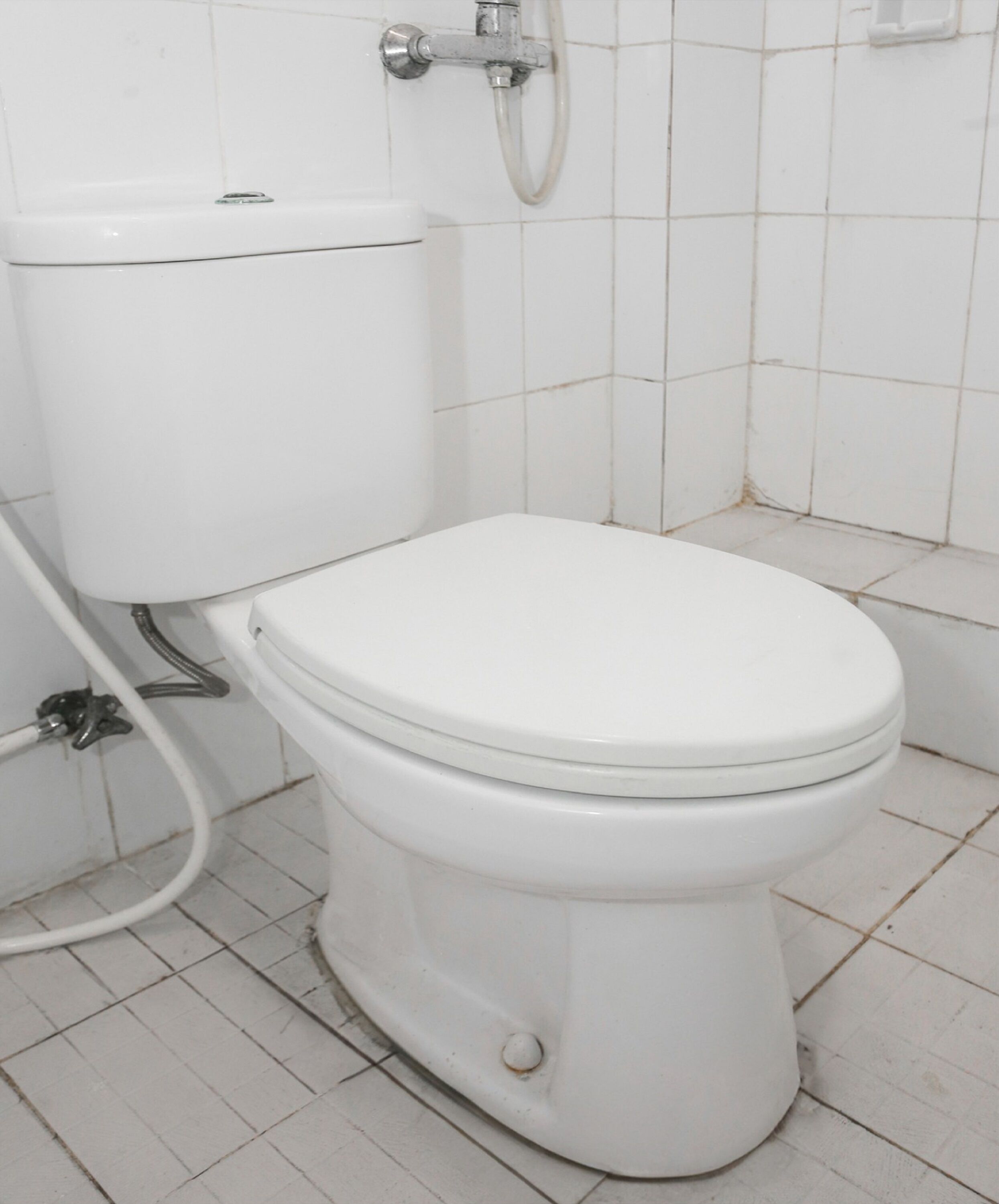 A white toilet with a tank, a visible pipe, and a wall-mounted faucet.