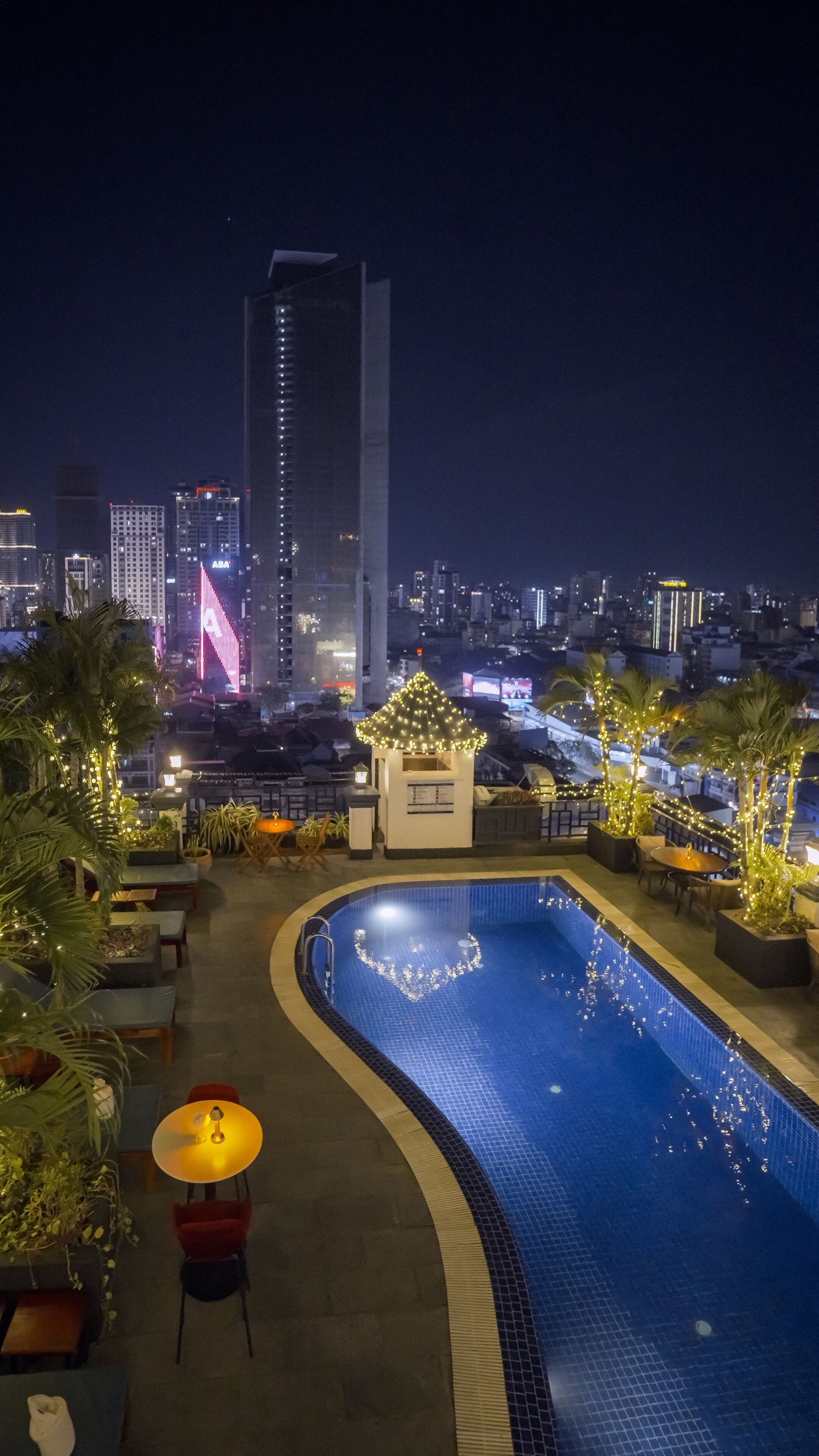 Ein Pool auf einem Dach bei Nacht mit einer Stadtansicht im Hintergrund.