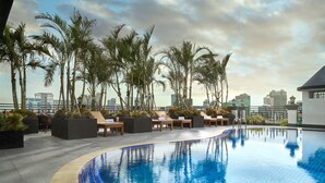 A rooftop pool with lounge chairs and palm trees, surrounded by city buildings. - Caravan Hotel by EHM (Phnom Penh)