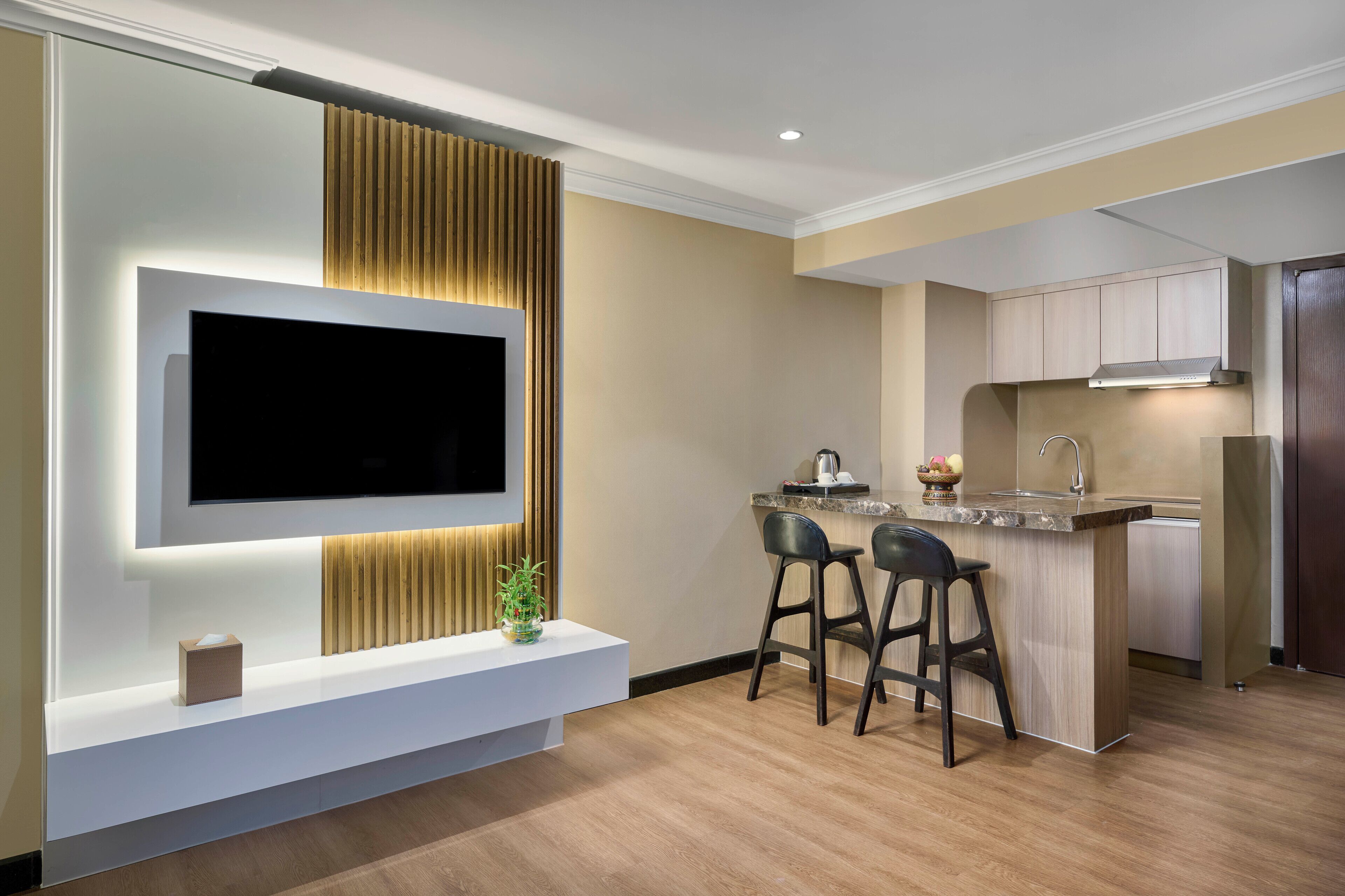 A modern kitchen with a built-in TV, wooden panel accent, and a bar area with stools.